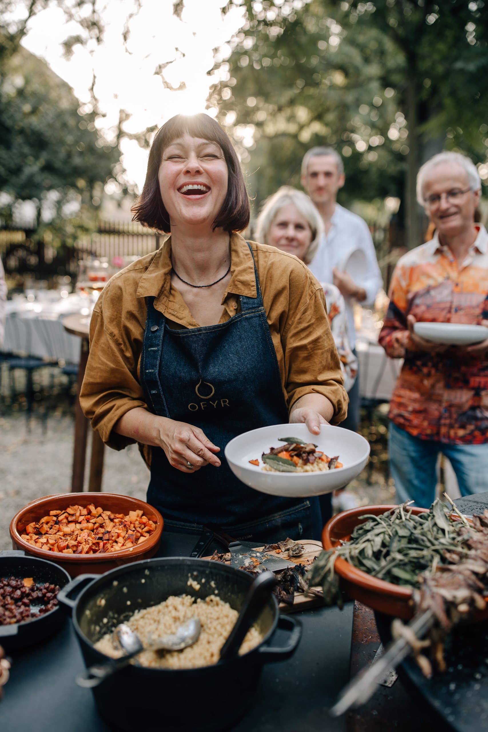 Tina von Tinchens Kitchen lacht beim Anrichten am Feuer
